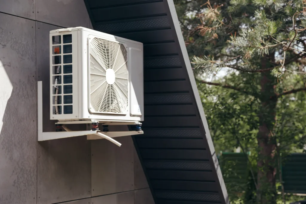 An outdoor AC unit mounted on the side of a building with trees in the background.